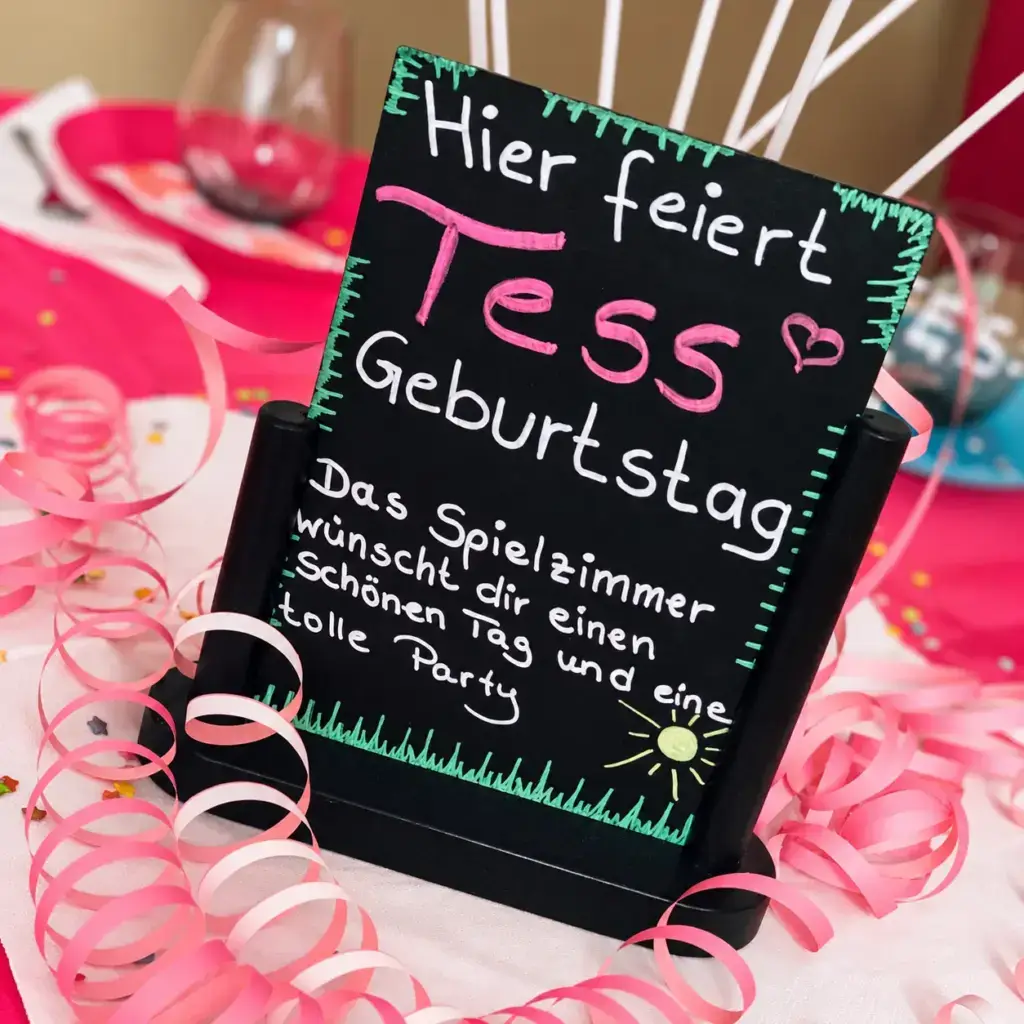 Persönlicher Geburtstagsgruß auf einer Kreidetafel zwischen rosa Luftschlangen