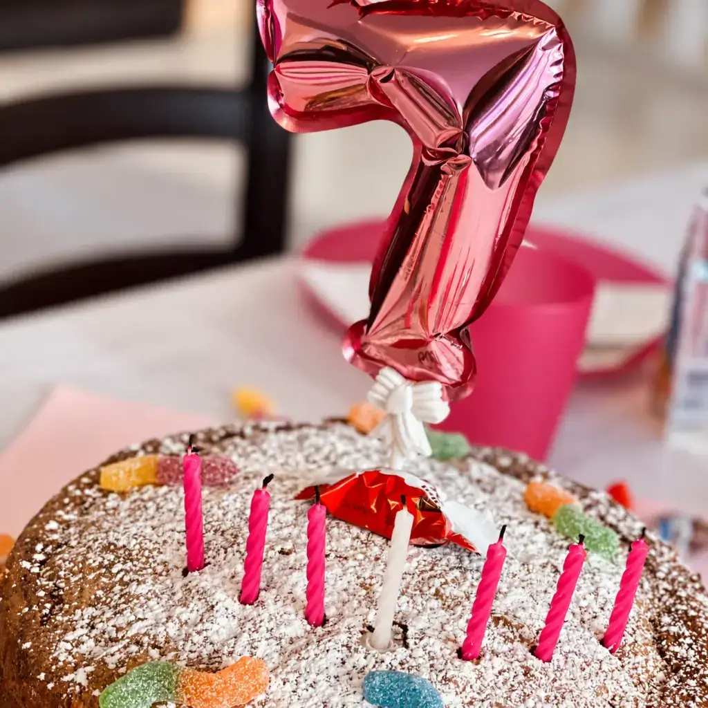 Geburtstagskuchen mit Kerzen, bunten Süßigkeiten und einem Zahlenballon zum siebten Geburtstag
