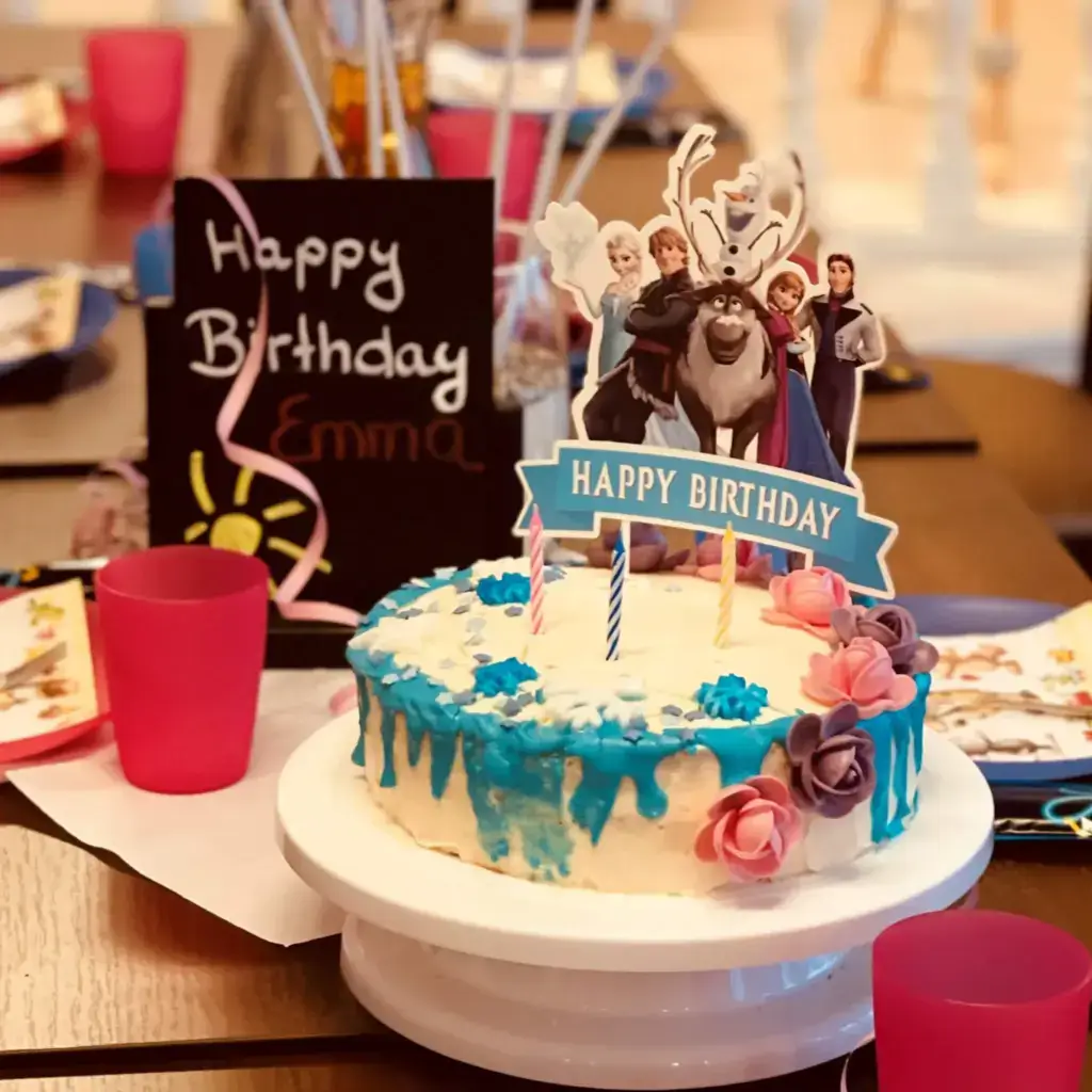 Frozen-Geburtstagstorte mit Figuren, Kerzen und rosa und lila Blüten auf dem Geburtstagstisch
